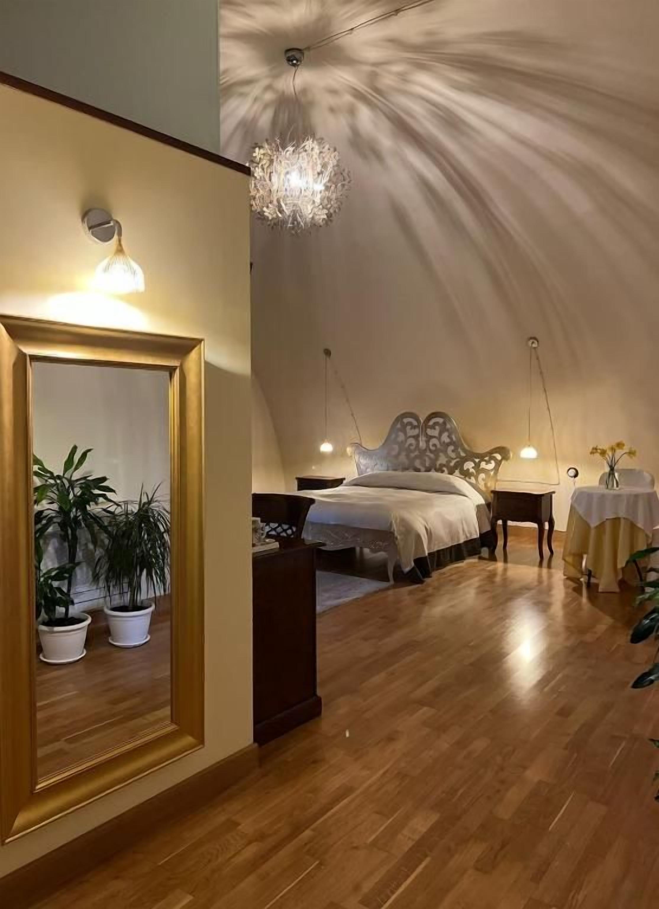 A bedroom with a large bed, bedside tables, a mirror, and a chandelier.