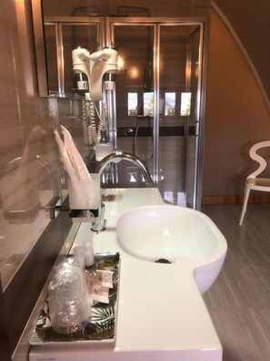 A modern bathroom with a large white sink, a glass shower enclosure, and a white chair.