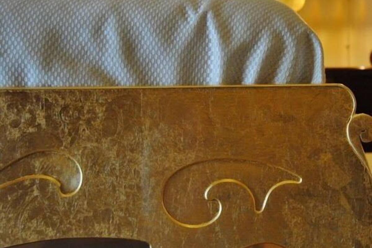 A bed with a textured white cover and a gold headboard with carved details.