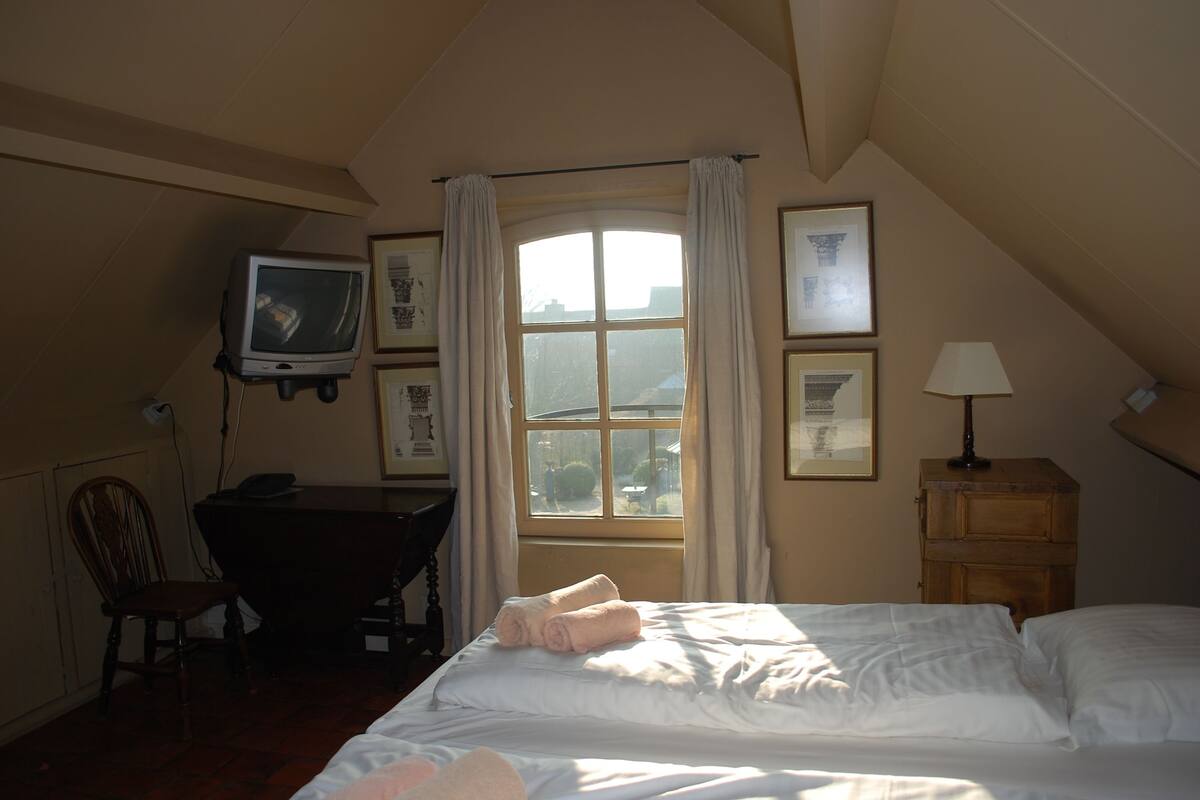 A bedroom with a bed, a desk, a television, and a window with curtains.