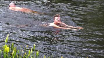 Two people swimming in a natural water body surrounded by greenery.