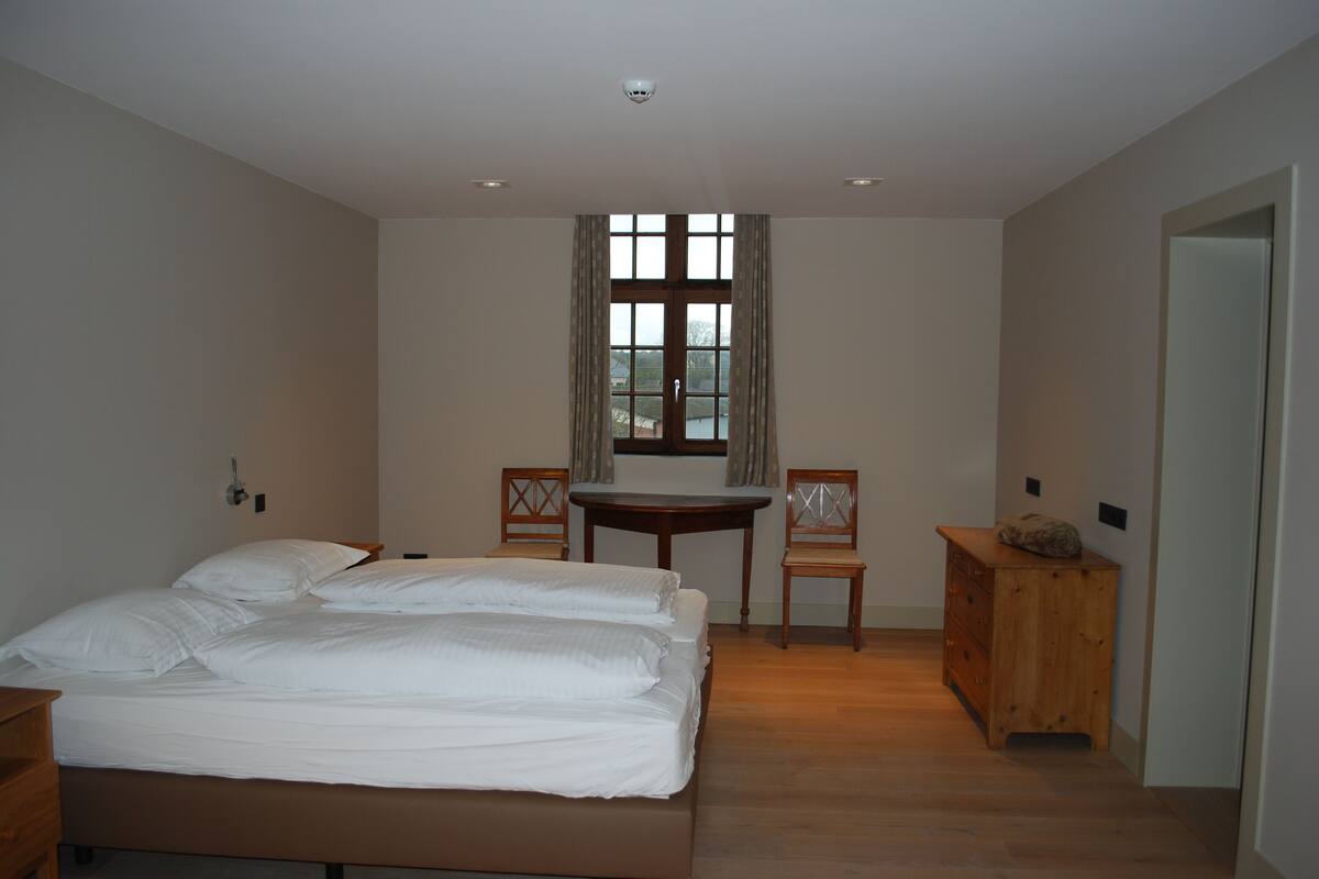 A bedroom with a large bed, a small table, two chairs, and a wooden dresser.
