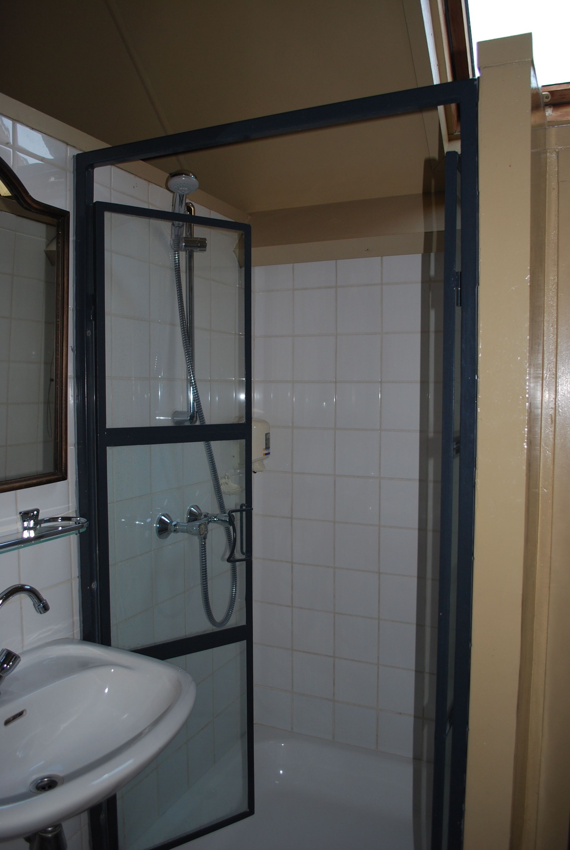 Ett badrum med en dusch som är avskärmad med glasväggar, ett handfat och en spegel.