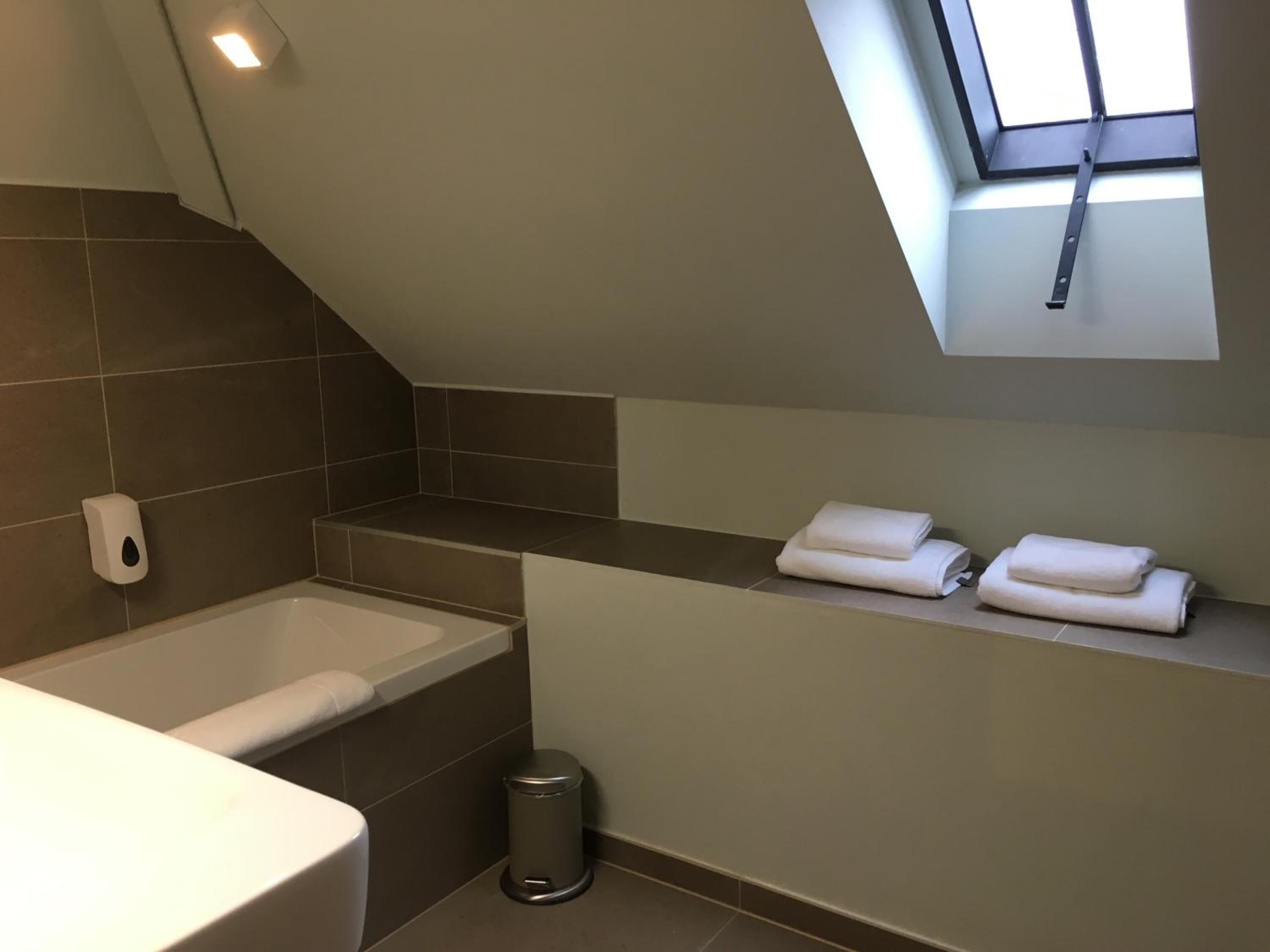 A modern bathroom with a skylight, a bathtub, a toilet, and a trash bin.