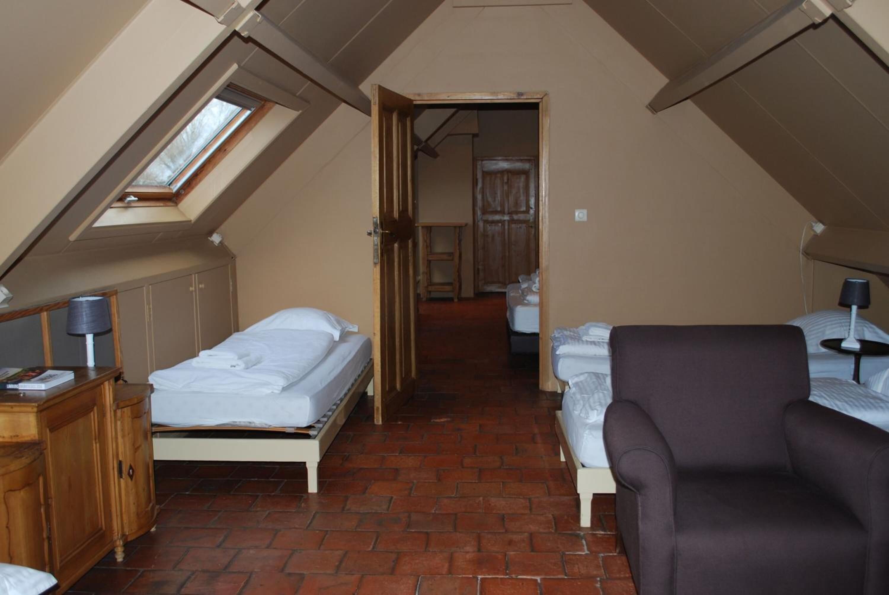Een kleine kamer onder de dakrand, met twee bedden, een houten kast en een stoel.