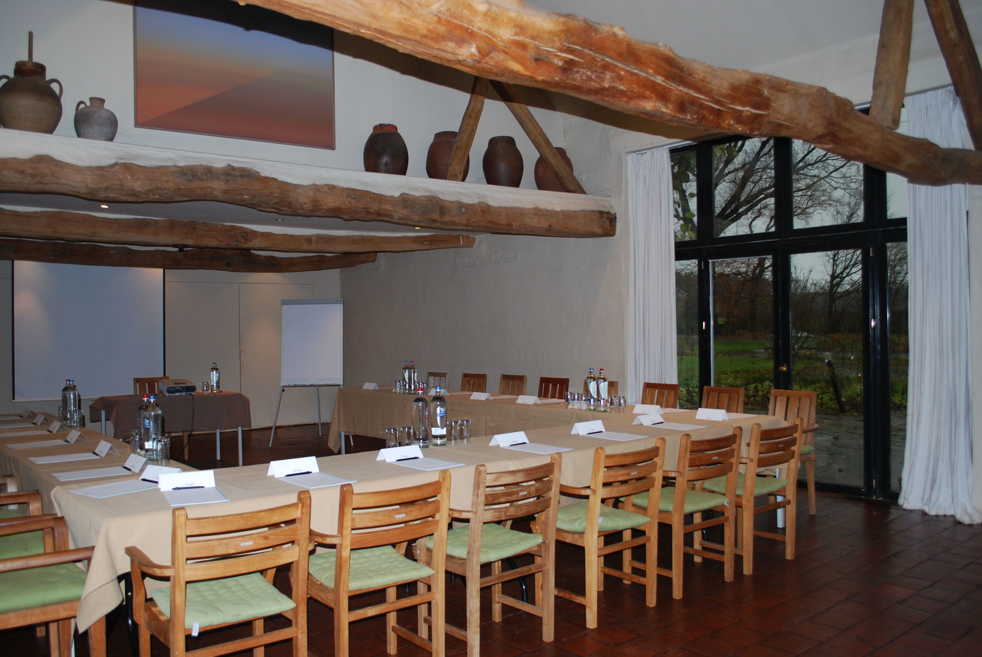 A conference room with a long table, wooden chairs, and a rustic ceiling beam.