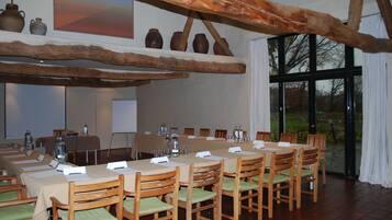 A conference room with a long table, wooden chairs, and a rustic ceiling beam.