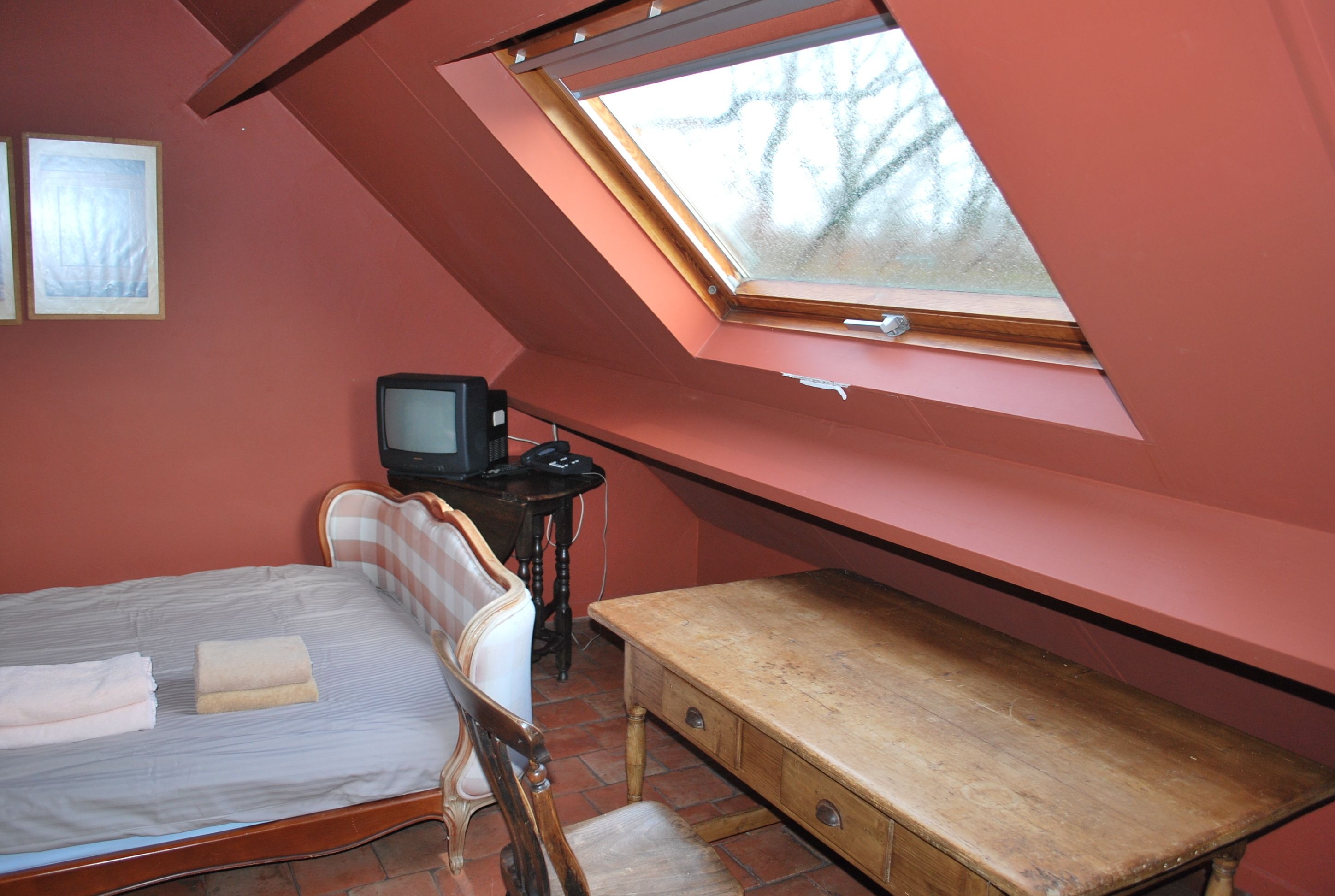 Une pièce comprenant un lit, un bureau en bois, une télévision et une lucarne.