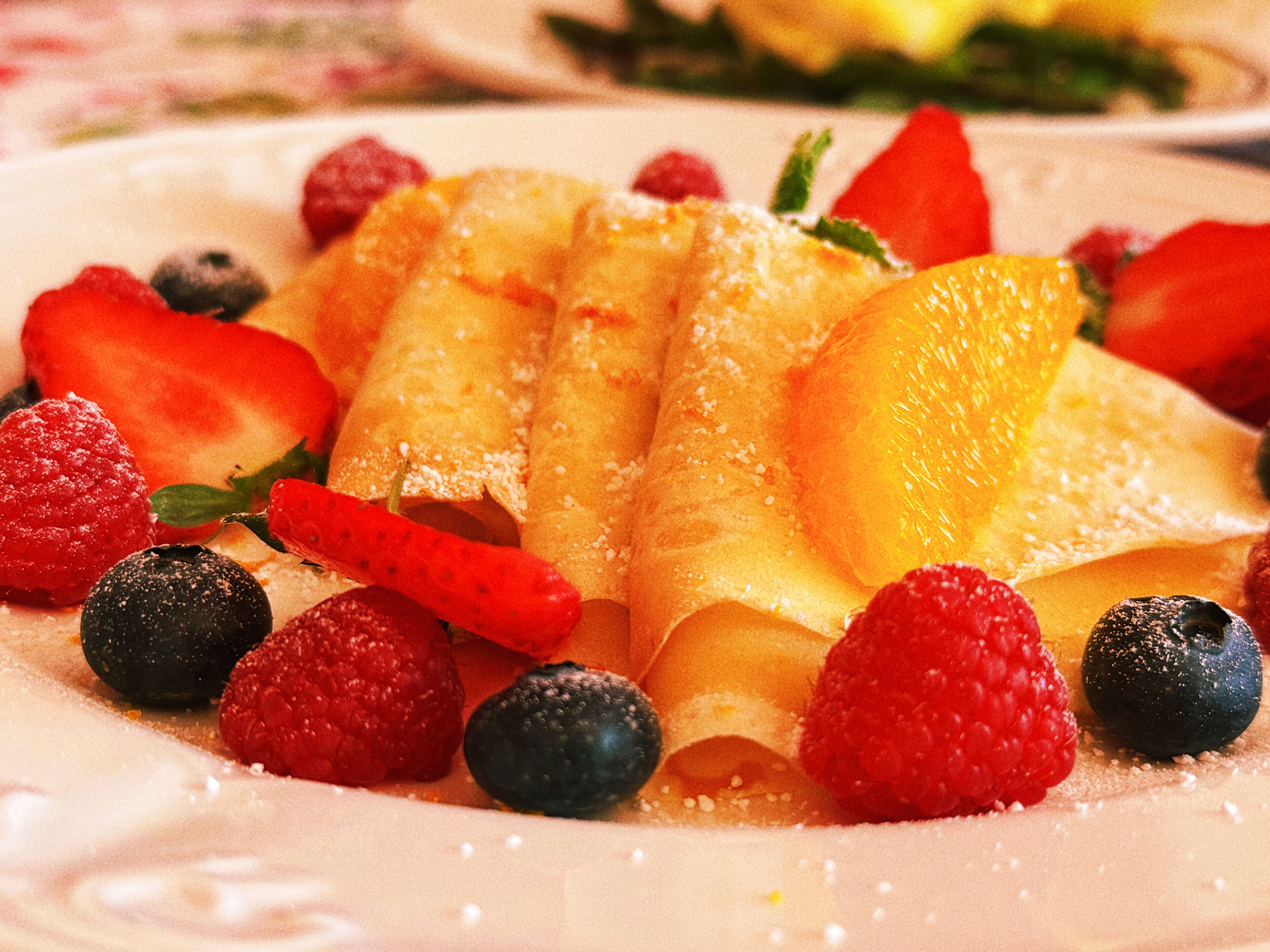 A dessert plate with rolled crepes, strawberries, blueberries, and a red chili pepper.
