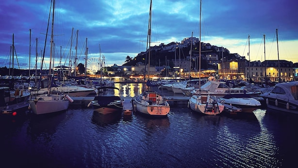 A marina with multiple boats docked, a Ferris wheel in the background, and buildings with lights on. - The Robin Hill Hotel (Torquay)
