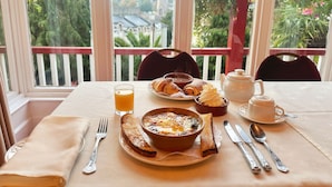 A breakfast setting with croissants, a bowl of eggs, and a teapot on a table with a view of greenery and a church spire through large windows. - The Robin Hill Hotel (Torquay)