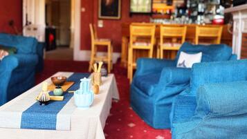 Ein gemütliches Wohnzimmer mit blauen Sofas, einem Couchtisch mit Teeservice und einer Bar im Hintergrund.