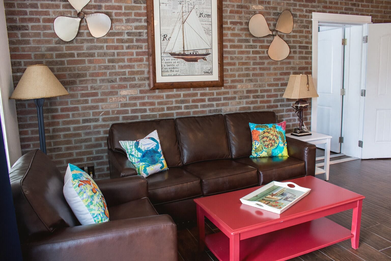 Un salon avec un canapé en cuir marron, deux coussins colorés, une table basse rouge et une carte encadrée accrochée au mur.