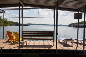 A covered dock with a bench and Adirondack chairs, overlooking a calm lake with distant land and dock structures. - Stormy Point Village Lakeside (Branson)