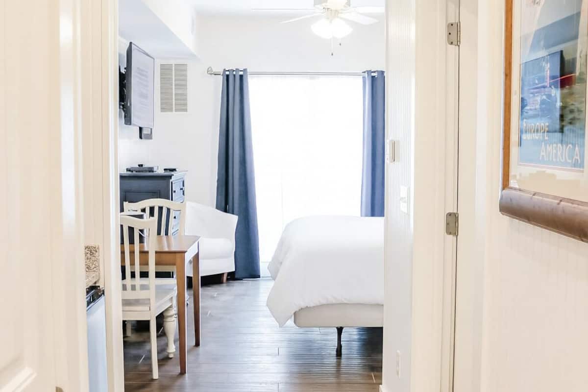 Una habitación de hotel con cama, escritorio con silla, televisor y ventilador de techo.