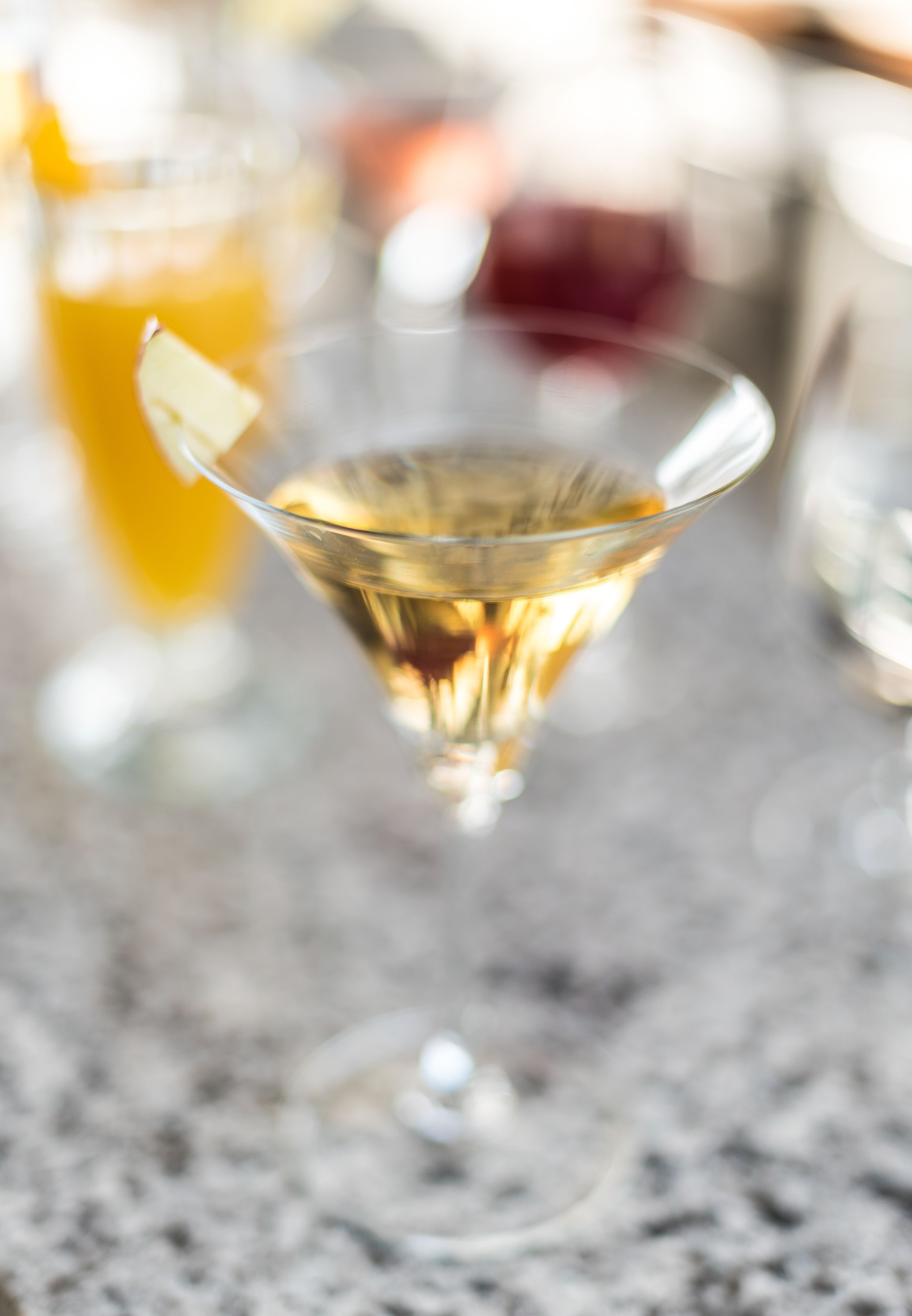 A close-up of a martini glass with a lemon twist on a marble countertop.