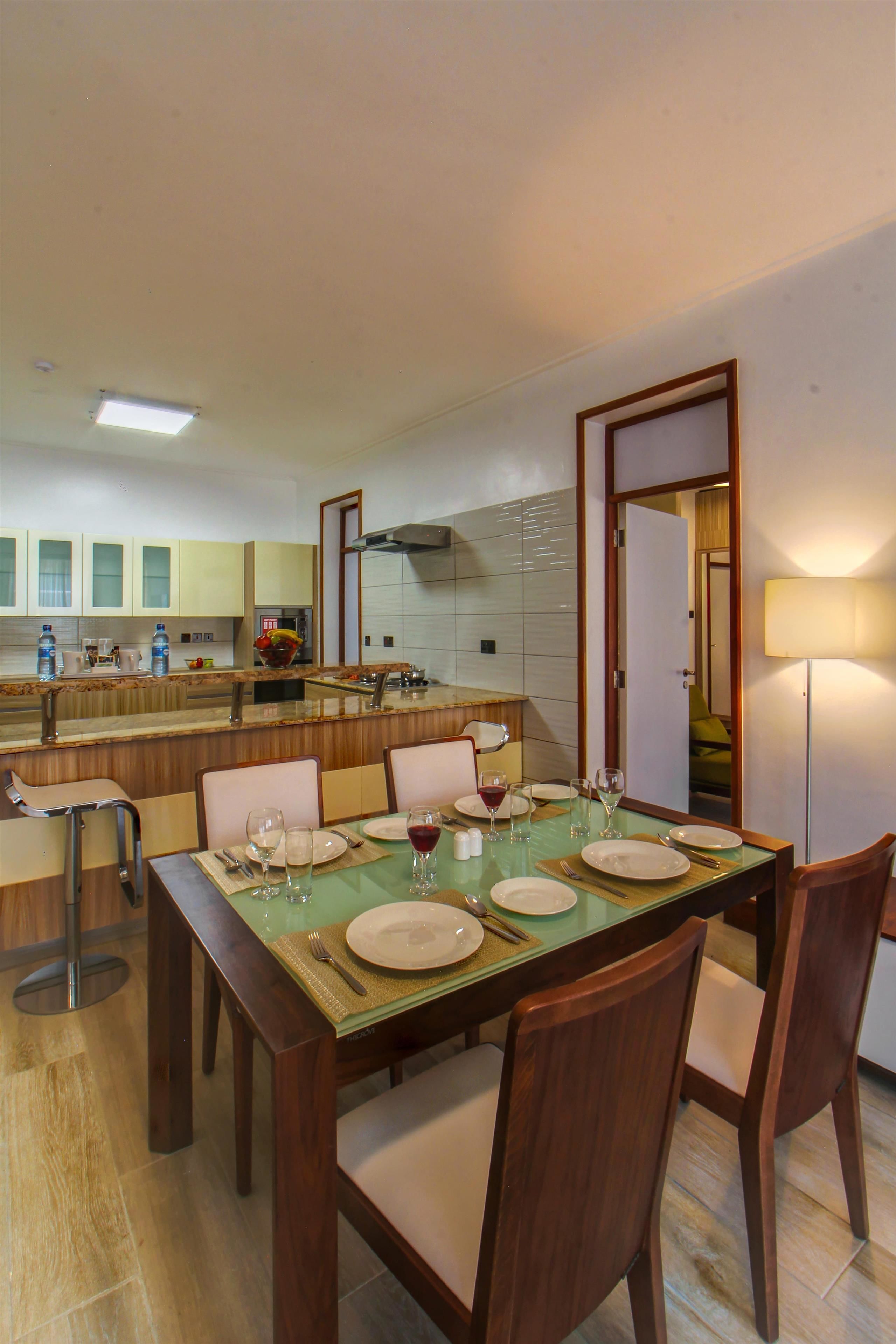 A dining area with a table set for four, a kitchen in the background, and a mirror reflecting the room.
