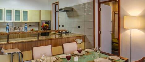 A dining area with a table set for four, a kitchen in the background, and a mirror reflecting the room.