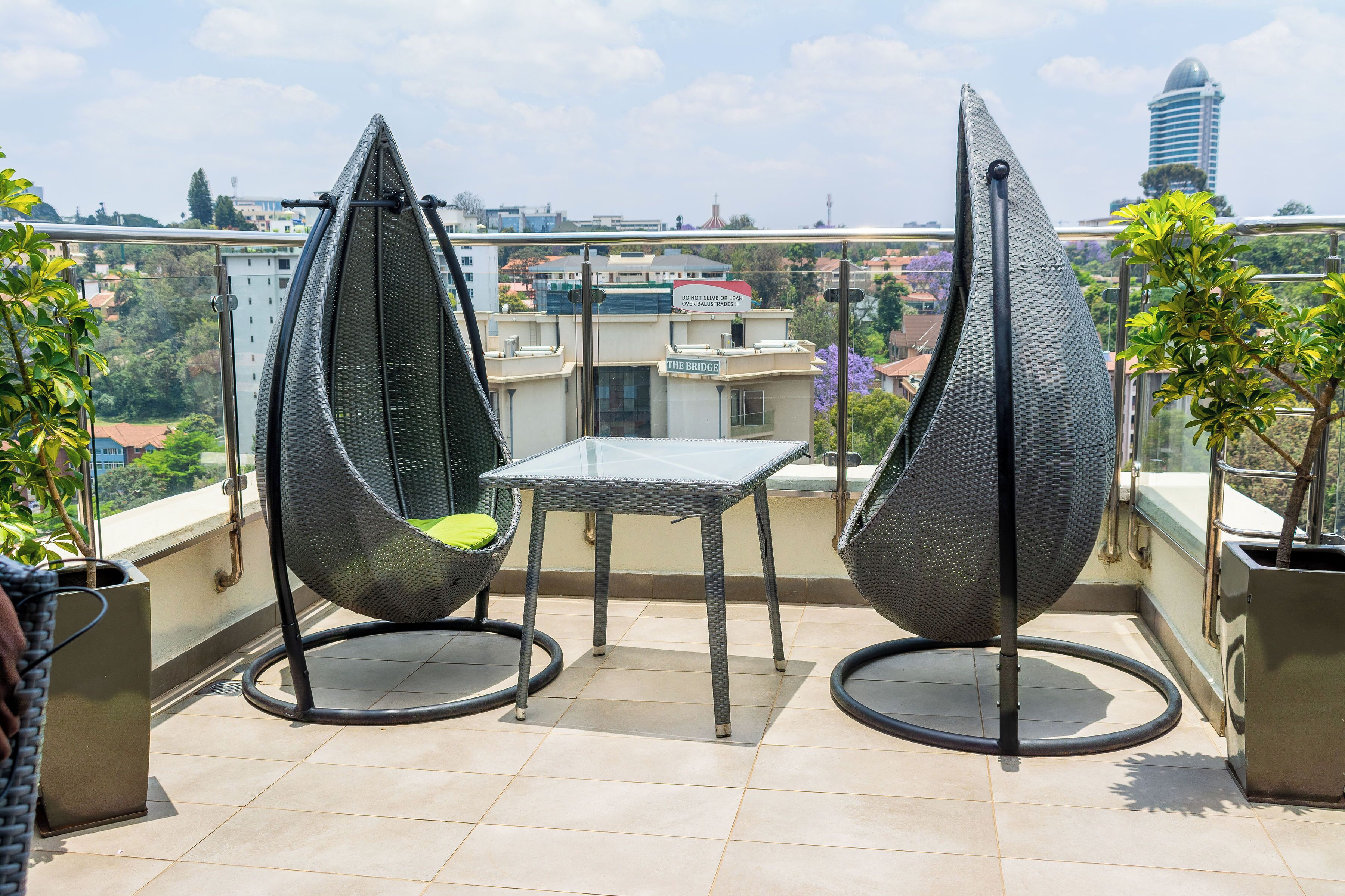 Een balkon met twee zwarte wicker stoelen, een tafeltje en potten met planten.