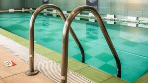Une piscine intérieure avec des parois en verre transparent, des échelles métalliques et une verrière au-dessus.