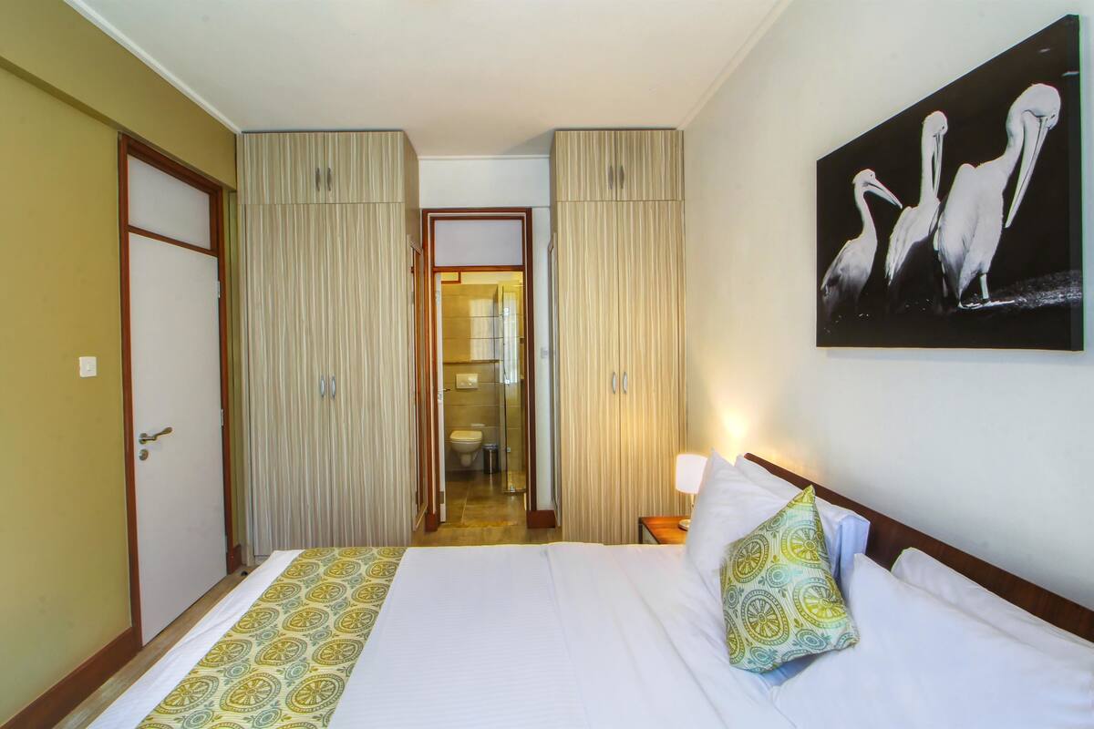 Une chambre d’hôtel avec un lit, un tableau représentant des oiseaux accroché au mur et une salle de bain visible à travers une porte.