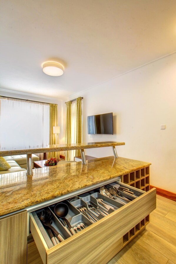 Een moderne keuken met een granieten aanrechtblad, een inbouw lade voor keukengerei, een flatscreen televisie aan de muur en een eethoek met een tafel en stoelen.
