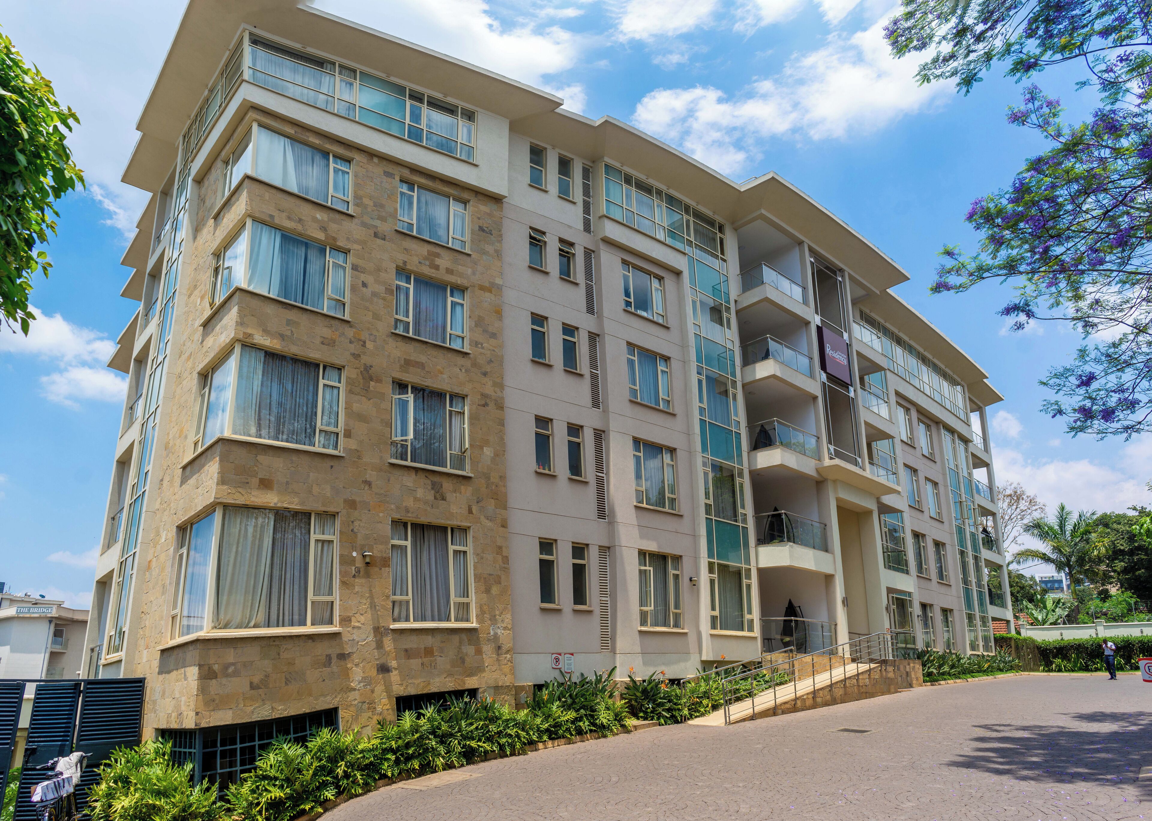 A multi-story hotel with a stone facade, multiple balconies, and a landscaped entrance area.