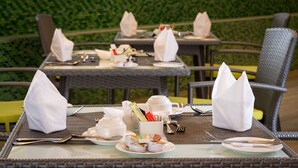 Eettafels buiten met witte servetten, theekoppen en borden, op de achtergrond een groene haag.