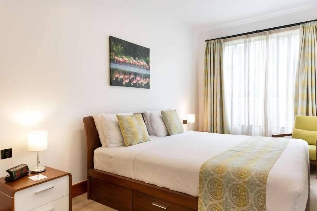 Une chambre d’hôtel avec un lit, des tables de chevet, un bureau avec une lampe, une chaise et un tableau au mur.