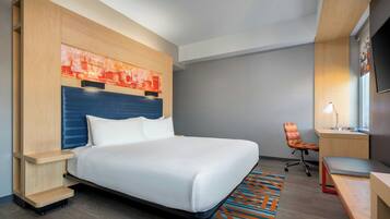A modern hotel room with a large bed, a desk, a chair, and a TV.