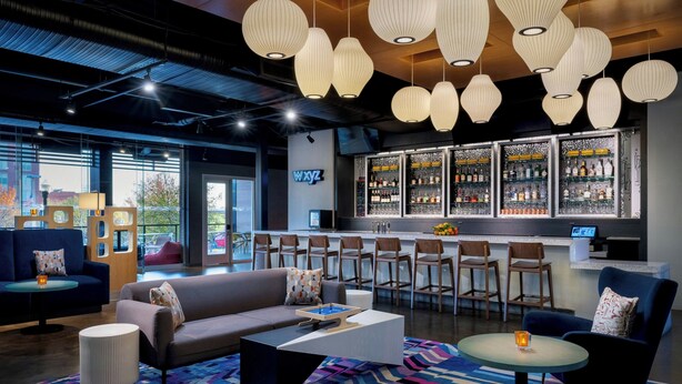 A modern bar area with a bar counter, seating, and a variety of bottles. - Aloft by Marriott Columbia Downtown (Columbia)