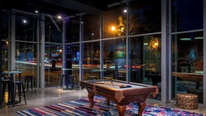 A pool table in a modern indoor setting with large windows, a patterned rug, and bar stools. - Aloft by Marriott Columbia Downtown (Columbia)