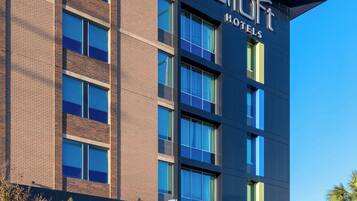 A modern hotel building with a prominent 'Aloft Hotels' sign, featuring a brick facade and large windows.