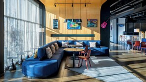 A modern lounge area with a blue sofa, round tables, and artwork on the walls. - Aloft by Marriott Columbia Downtown (Columbia)