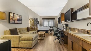 A compact hotel room with a sofa, a small desk, a bed, and a TV.