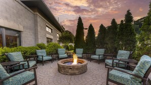 A fire pit surrounded by outdoor seating, a stone patio, and a building with large windows.
