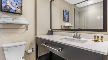 A modern bathroom with a toilet, sink, and mirror. There are towels on a shelf, and toiletries on the sink.