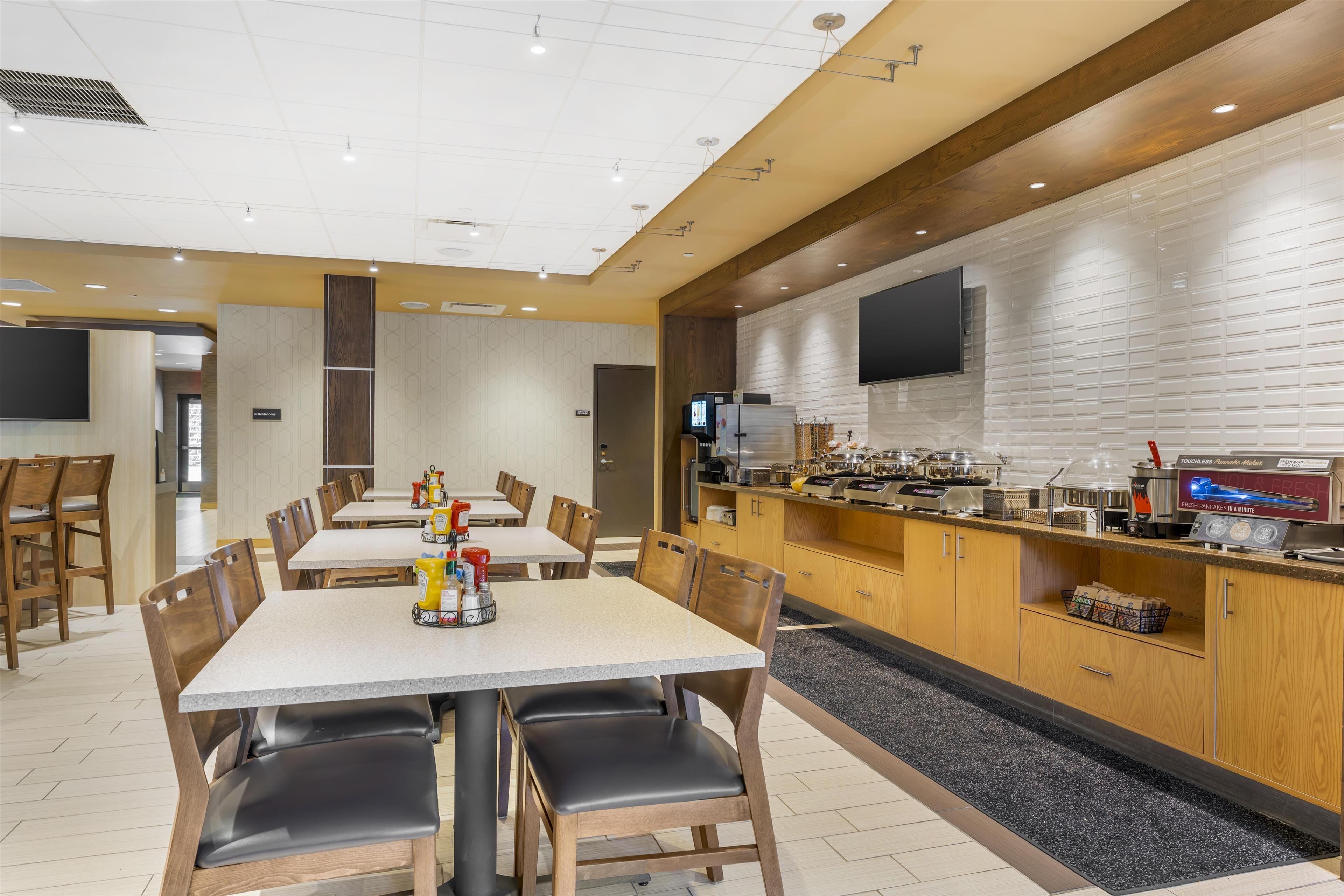 A modern restaurant with a long counter, multiple tables, and chairs.