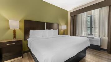 A hotel room with a large bed, two bedside tables with lamps, a window with curtains, and an air conditioning unit.
