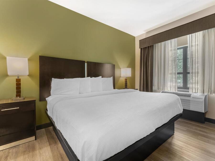 Habitación de hotel con una cama grande, dos mesitas de noche con lámparas, una ventana con cortinas e un equipo de aire acondicionado.