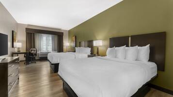 A hotel room with two beds, a desk, a chair, and a large window with curtains.
