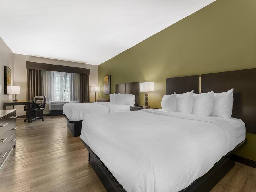 A hotel room with two beds, a desk, a chair, and a large window with curtains.