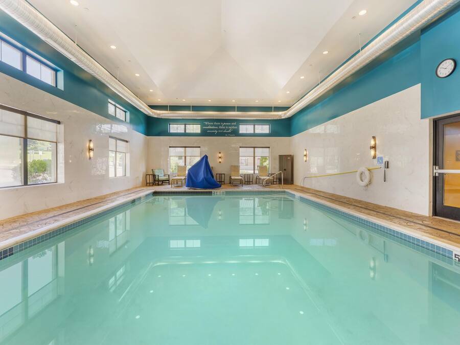 Una gran piscina interior con agua cristalina, rodeada de paredes con ventanas y un reloj.