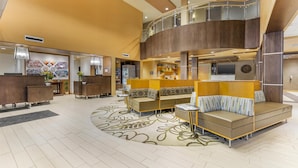 A spacious lobby with a high ceiling, a reception desk, seating area, and a staircase leading to an upper level.