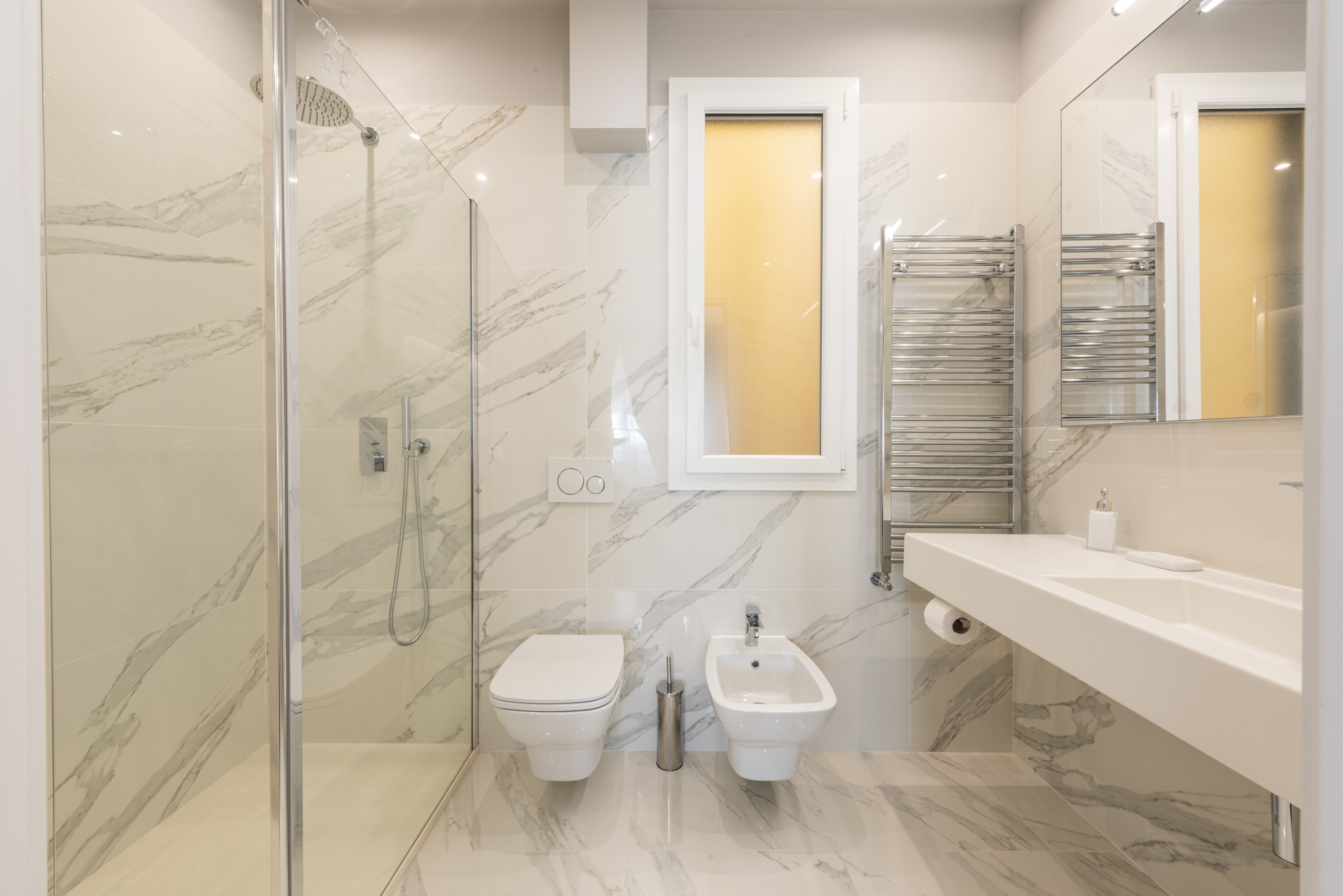 A modern bathroom with a glass-enclosed shower, a toilet, a bidet, and a vanity with a mirror.