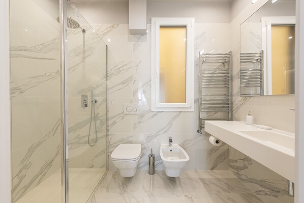 A modern bathroom with a glass-enclosed shower, a toilet, a bidet, and a vanity with a mirror.