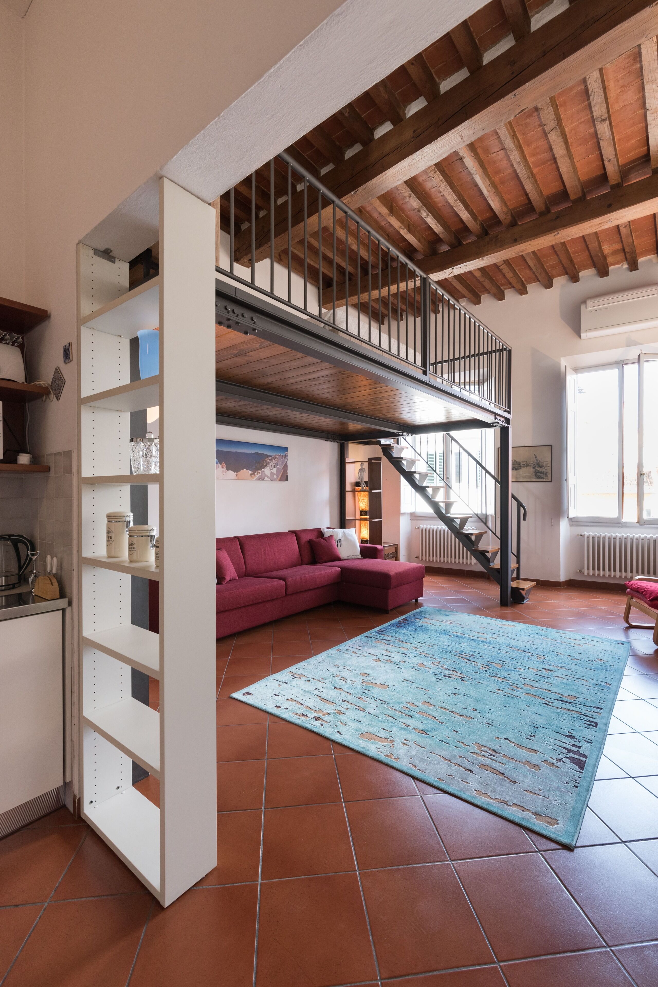 A spacious living area with a red sofa, a blue rug, and a staircase leading to an upper level.