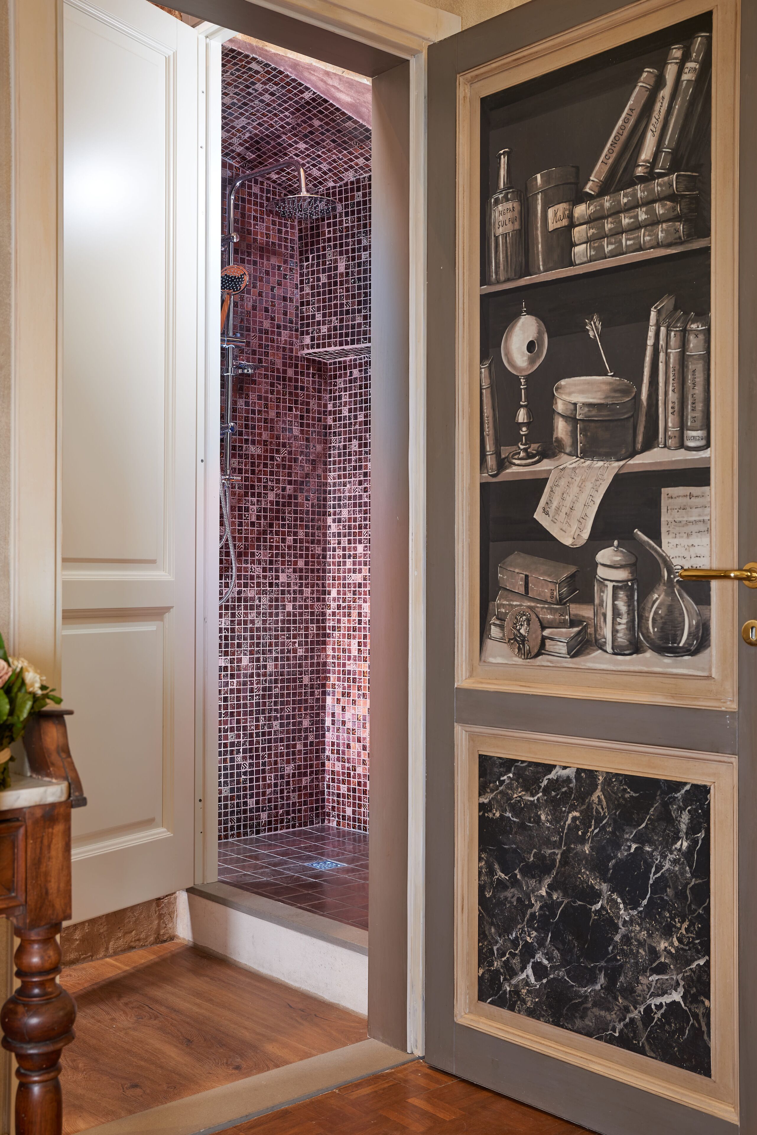 Un passage orné d’un mur recouvert de mosaïques, d’un cadre de porte en bois et d’une étagère où sont posés des livres et des objets décoratifs.
