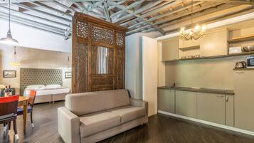 Una sala moderna con sofá, mesa de comedor y sillas, una zona de cocina con armarios y electrodomésticos, y un separador decorativo de madera.
