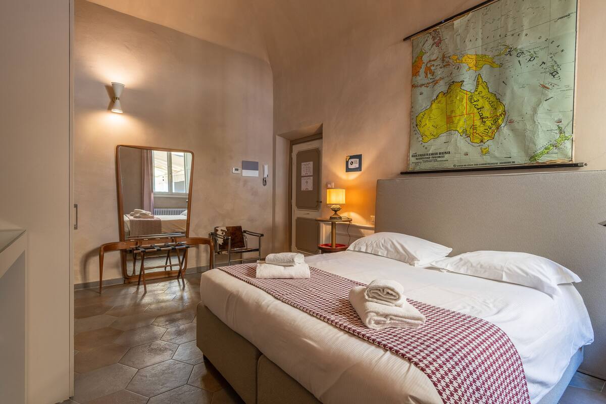 A hotel room with a large bed, a desk, a chair, a map on the wall, and a bathroom door.